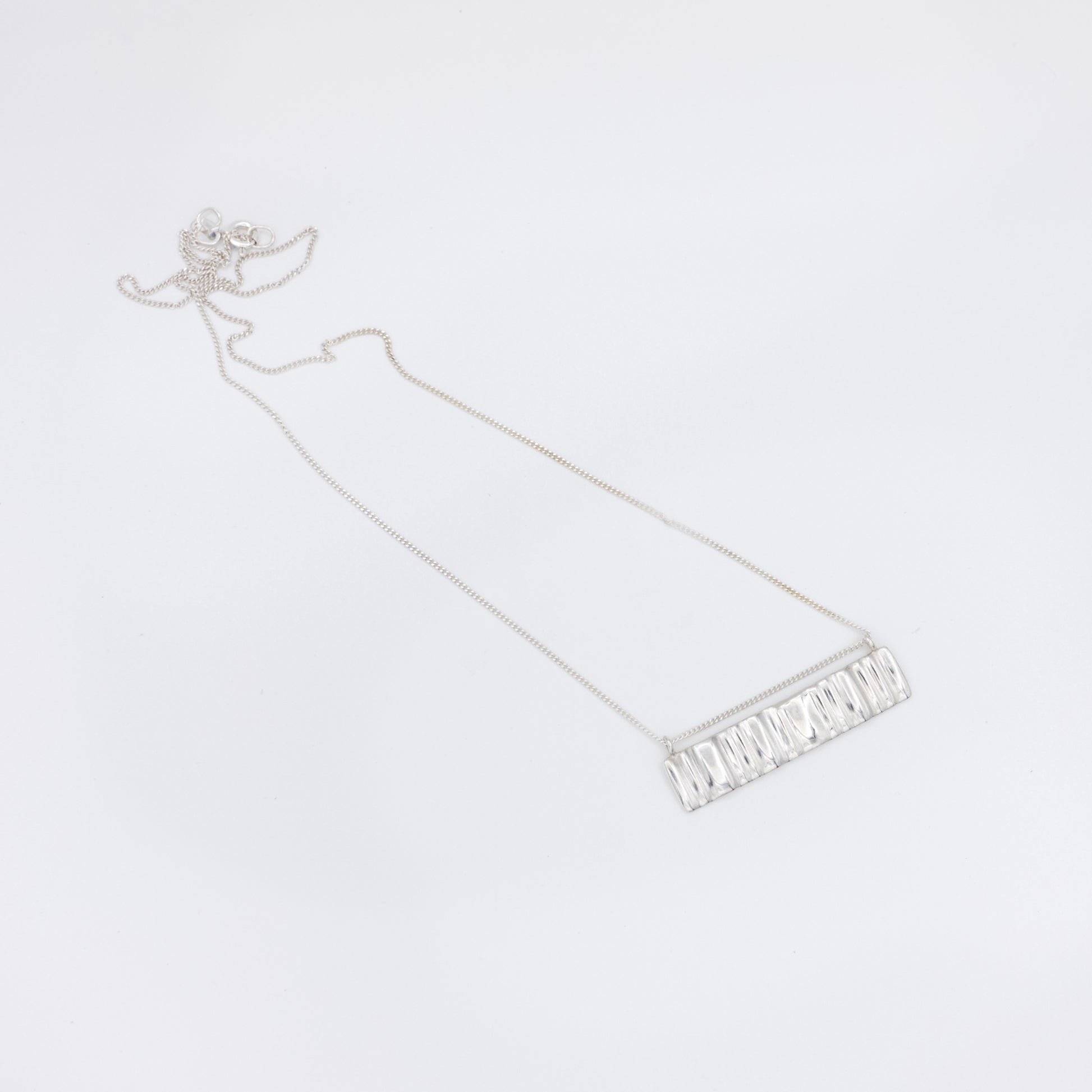 Top view of the Wave silver necklace with a textured rectangular pendant, pictured on a light plain background.